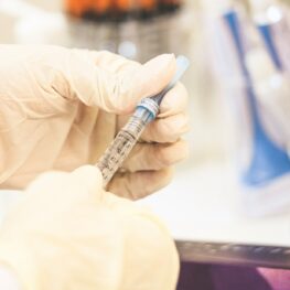 Dentist wearing white gloves holding a botox needle